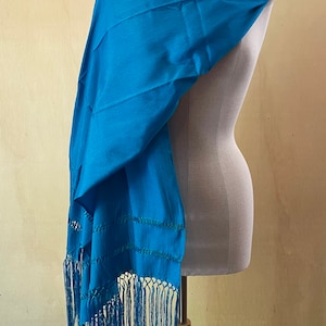 May include: A teal blue shawl with fringe. The shawl is draped over a mannequin.