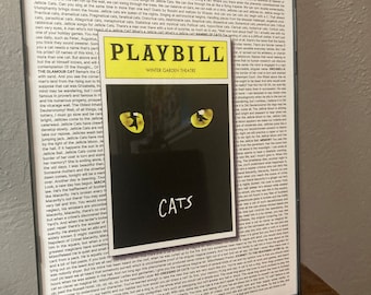 May include: A framed Playbill for the musical Cats, featuring a black cat with green eyes. The Playbill is for the Winter Garden Theatre. The text on the Playbill includes the title "Cats" and the words "Journey to the Heaviside Layer".