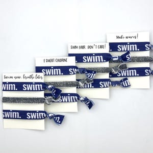May include: Set of six blue and silver hair ties with the word "swim" printed on them. Each hair tie is packaged on a white card with a different swim-themed saying. The sayings are "Swim now, breathe later", "I sweat chlorine", "Swim hair, don't care!" and "Make waves!"