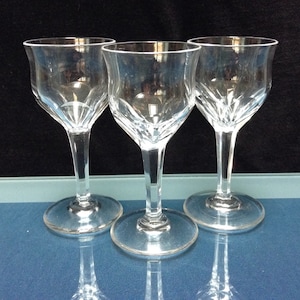 May include: Three clear glass wine glasses with a cut crystal design. The glasses are arranged in a row on a blue surface.