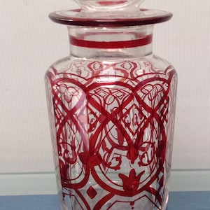 Peut inclure: Une bouteille en verre transparent avec un couvercle rayé rouge et blanc. La bouteille a un motif géométrique rouge sur le corps.