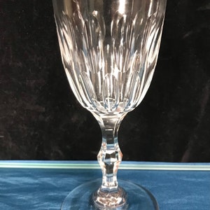 May include: A clear glass wine glass with a cut crystal design. The glass has a tall, slender stem and a wide, round base.