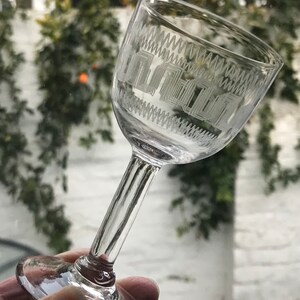 Może przedstawiać: Szklanka do shotów wykonana z przezroczystego szkła z dekoracyjnym grawerowanym wzorem. Wzór przedstawia powtarzający się wzór geometrycznych kształtów.