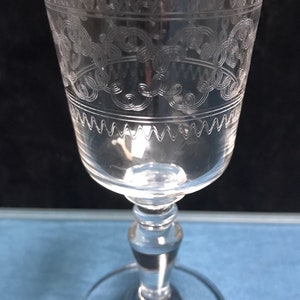 May include: A clear glass wine goblet with an etched design of a floral pattern around the top and bottom of the bowl. The goblet has a tall, slender stem and a wide, flat base.