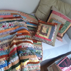 May include: A handmade quilt and pillows with a patchwork design. The quilt features strips of various patterned fabrics in shades of blue, orange, brown, and floral prints. The pillows have similar patterns and colors.