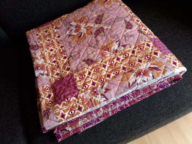 Puede incluir: Un edred&oacute;n plegado con un patr&oacute;n floral y geom&eacute;trico en tonos rosa, marr&oacute;n y morado. El edred&oacute;n presenta un dise&ntilde;o acolchado y est&aacute; doblado cuidadosamente, mostrando su intrincado patchwork y paleta de colores.