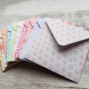 May include: A stack of colorful patterned envelopes with a light blue envelope on top. The envelopes are folded and have a variety of floral and geometric designs.