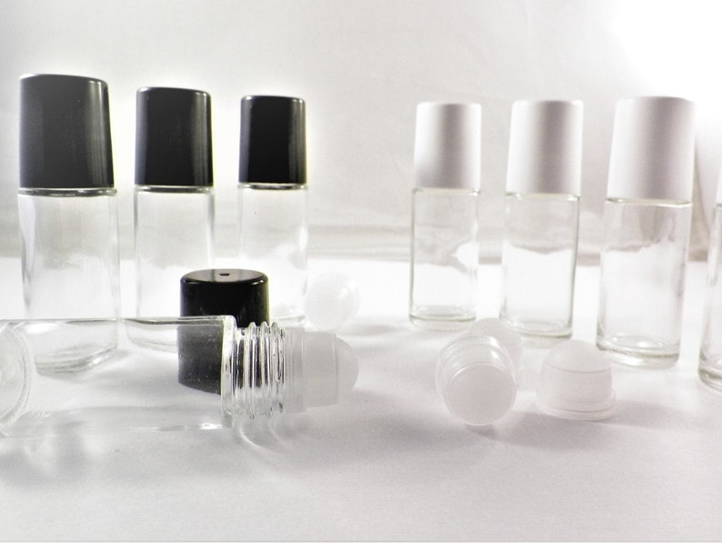 K&ouml;nnte beinhalten: Eine Sammlung von transparenten Glas-Rollflaschen mit schwarzen und wei&szlig;en Kappen. Einige Flaschen stehen aufrecht, w&auml;hrend andere liegen. Die Flaschen sind leer und bereit, mit &auml;therischen &Ouml;len oder anderen Fl&uuml;ssigkeiten gef&uuml;llt zu werden.