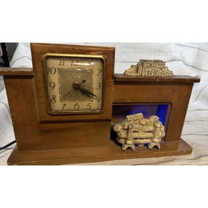 May include: A vintage wooden clock with a square face and gold-colored numerals. The clock has a decorative fireplace design with a small sculpture on top and another inside the fireplace. The clock is brown and has a United logo.