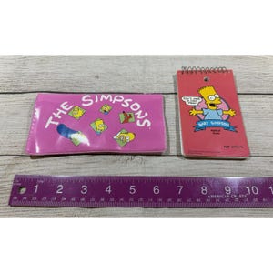 May include: A pink wallet and a red notepad featuring The Simpsons characters. The wallet has the show's logo and character graphics. The notepad features Bart Simpson with the text "Don't Have a Cow, Man!" and "Radical Dude."