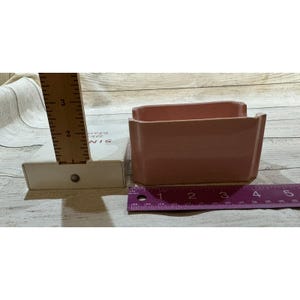 May include: A pair of rectangular, light pink ceramic containers. Each container is approximately 4 inches long. The containers are placed on a wooden surface next to a ruler.