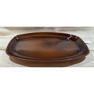 May include: A brown, rectangular ceramic serving platter with rounded corners. The platter has a glossy finish and is empty. The background is a light-colored wooden surface.