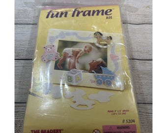 以下が含まれることがあります： 透明なプラスチックパッケージに入った黄色のFun Frameキット。パッケージには赤ちゃんの写真が印刷されており、テディベア、木馬、乳母車の装飾用切り抜きが含まれています。10cm x 15cmの写真を収納可能で、番号は#5204です。