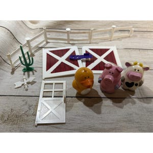 Può includere: Un set da gioco per la fattoria con una recinzione bianca, porte di fienile rosse e una porta bianca. Il set include un'anatra gialla, un maiale rosa e una mucca con macchie nere. Sono inclusi anche un cactus verde e una banderuola bianca.