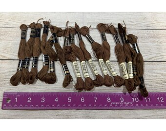 以下が含まれることがあります： 番号358が印刷された黒い紙ラベルが付いた、茶色の刺繍糸の束が14個あります。これらの束は、センチメートル単位の目盛りが付いた30cmの紫色の定規の上に水平に並べられています。