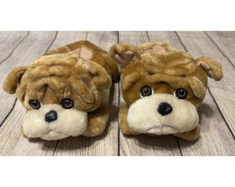 以下が含まれることがあります： ブルドッグのぬいぐるみスリッパのペア。スリッパは茶色で、タンと白のアクセントがあり、黒い鼻と暗い目があります。スリッパはブルドッグの顔に似せてデザインされています。