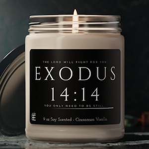 May include: A lit, off-white candle in a clear glass jar with a silver lid. The black label features the text "EXODUS 14:14" and "THE LORD WILL FIGHT FOR YOU: YOU ONLY NEED TO BE STILL." The candle is 9 oz and scented with Cinnamon Vanilla.