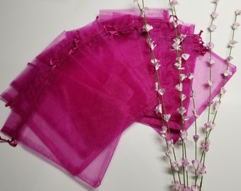 May include: A set of six pink organza gift bags with satin ribbon ties. The bags are arranged in a fan shape and are lying on a white surface.