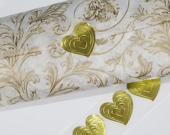 Può includere: Adesivi dorati a forma di cuore con un design in rilievo. Gli adesivi sono su uno sfondo bianco con un motivo floreale dorato.