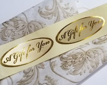 Può includere: Un rotolo di nastro color avorio con adesivi ovali in foglia d'oro che recitano "Un regalo per te".