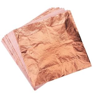 May include: A stack of copper-colored metallic leaf sheets. The sheets have a textured, wrinkled appearance, and are stacked on top of each other. The edges of the sheets are visible, showing the layered construction. The background is plain white.