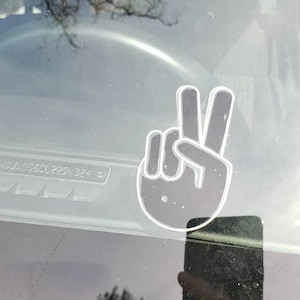May include: A peace sign sticker on a car window. The sticker is white with a black outline and is placed on the driver's side window.