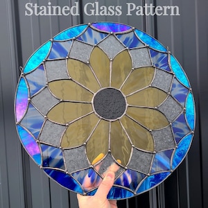 Puede incluir: Una ventana de vitral con un diseño de flor con un centro negro. La flor está rodeada por un patrón geométrico azul y gris.