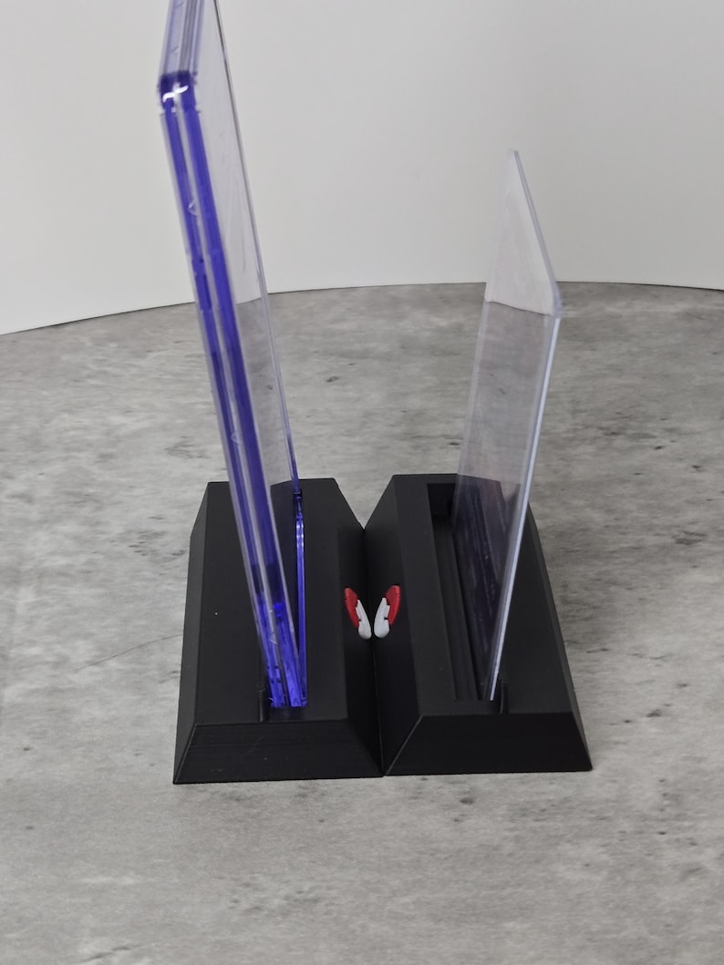 May include: A black, two-part display stand with clear, upright panels. The panels have a blue tint and are held in place by the stand. A small, red and white butterfly-shaped accent is between the panels.
