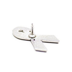 A silver pin with a ribbon-like shape attached to it, which appears to be a symbol of support or awareness for a cause.