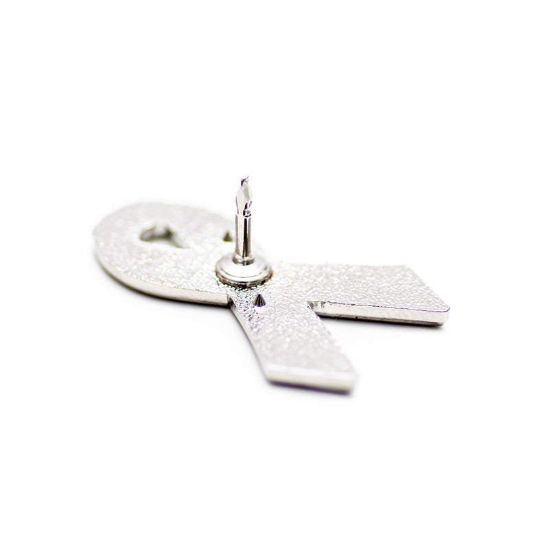 A silver pin with a ribbon-like shape attached to it, which appears to be a symbol of support or awareness for a cause.