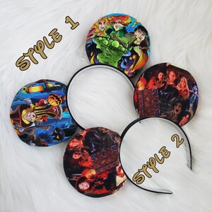 May include: Halloween-themed headband featuring two styles. Style 1 has a colorful design with witches and a green spaceship. Style 2 features a dark image of characters. The text "STYLE 1" and "STYLE 2" are in gold.