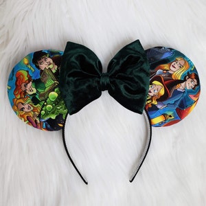 May include: A pair of mouse ears with a dark green velvet bow and character-themed ear designs. The ears feature colorful illustrations of characters on a white headband.