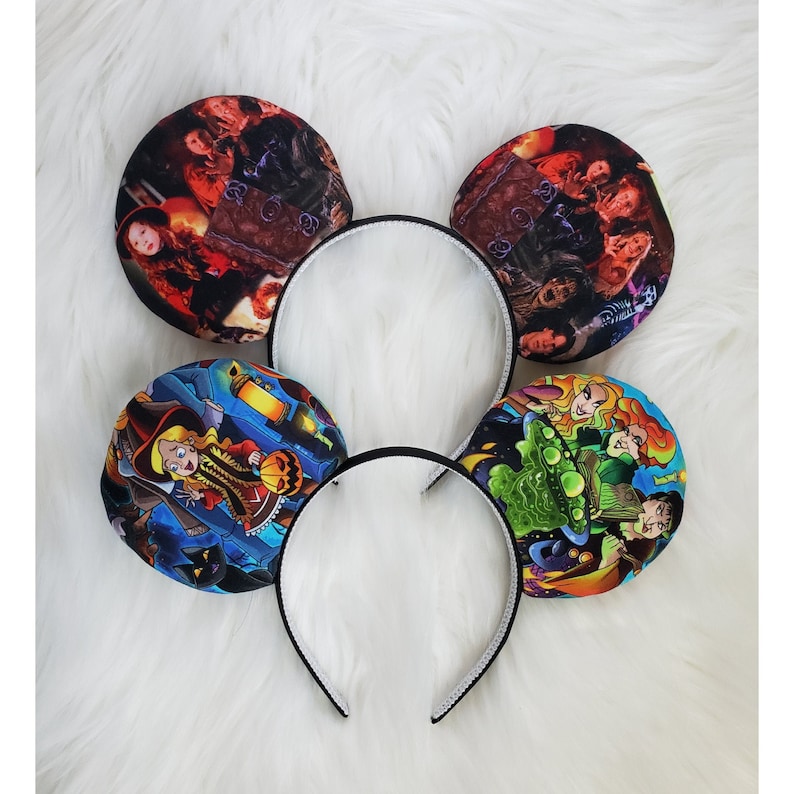 May include: Four black headbands with circular ear-shaped decorations. The decorations feature colorful illustrations of characters and scenes, likely from a movie or cartoon. The headbands are on a white, fluffy surface.