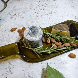May include: A green glass bottle repurposed as a serving tray with a round wheel of cheese, a block of cheese, almonds, and rosemary sprigs.