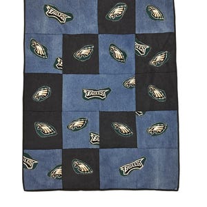 May include: A patchwork quilt featuring the Philadelphia Eagles logo and team name. The quilt is made of denim squares in shades of blue and black. The Eagles logo is a green and white eagle head.