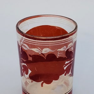 Puede incluir: Un vaso de vidrio transparente con un diseño floral rojo y blanco. El vaso tiene un borde rojo y una base roja.