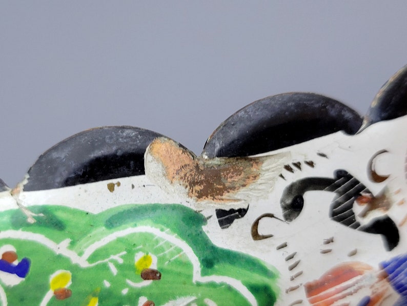 May include: Close-up of a ceramic dish with a scalloped edge. The dish is decorated with a green, white, and black floral design. The edge of the dish is painted black.