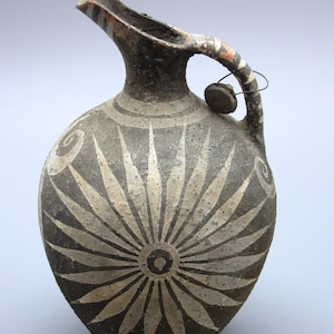 May include: A black and white ceramic jug with a starburst design. The jug has a handle with a small, round, clay tag attached.