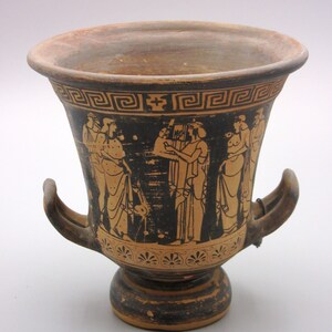 May include: Black and orange Greek pottery vase with two handles and a black and white painted scene of figures.