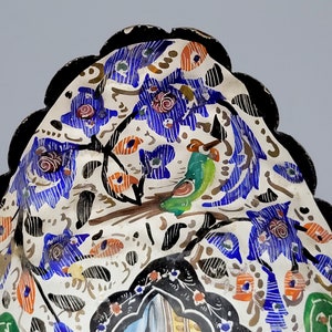 May include: A white ceramic bowl with a scalloped edge and a black rim. The bowl is decorated with a colorful floral pattern and a green bird.