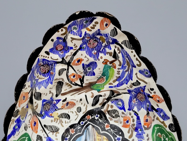 May include: A white ceramic bowl with a scalloped edge and a black rim. The bowl is decorated with a colorful floral pattern and a green bird.