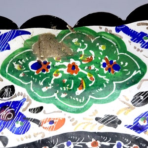 May include: A white ceramic dish with a scalloped edge and a colorful floral design. The design features green leaves, red and orange flowers, and blue accents.
