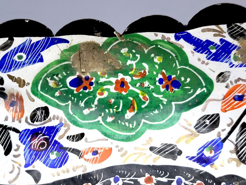 May include: A white ceramic dish with a scalloped edge and a colorful floral design. The design features green leaves, red and orange flowers, and blue accents.