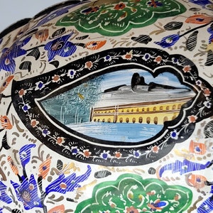 May include: A white ceramic bowl with a black and white floral design. The bowl has a blue and yellow scene painted in the center.
