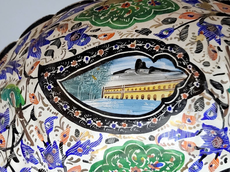 May include: A white ceramic bowl with a black and white floral design. The bowl has a blue and yellow scene painted in the center.