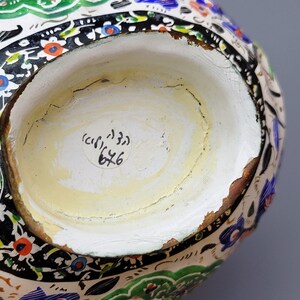 May include: The bottom of a white ceramic pitcher with a black, green, and blue floral design. A white sticker with the text "(c) 133 6x6" is on the bottom.