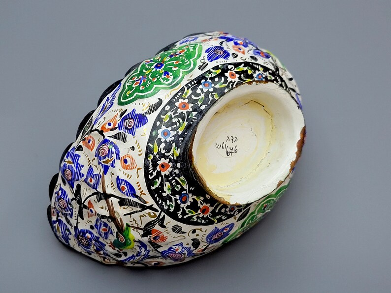 May include: A white ceramic bowl with a black, blue, green, and orange floral design. The bowl has a scalloped edge and a white interior with a handwritten inscription in black.