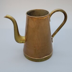 May include: A vintage copper and brass teapot with a long spout and a handle. The teapot has a worn, aged look and is a beautiful example of antique kitchenware.