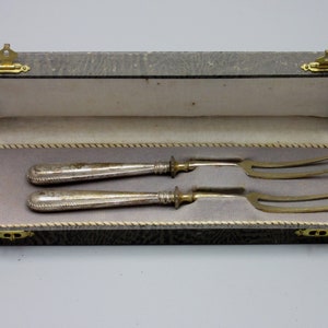 May include: Two silver serving forks with gold handles in a gray velvet lined box with brass clasps.