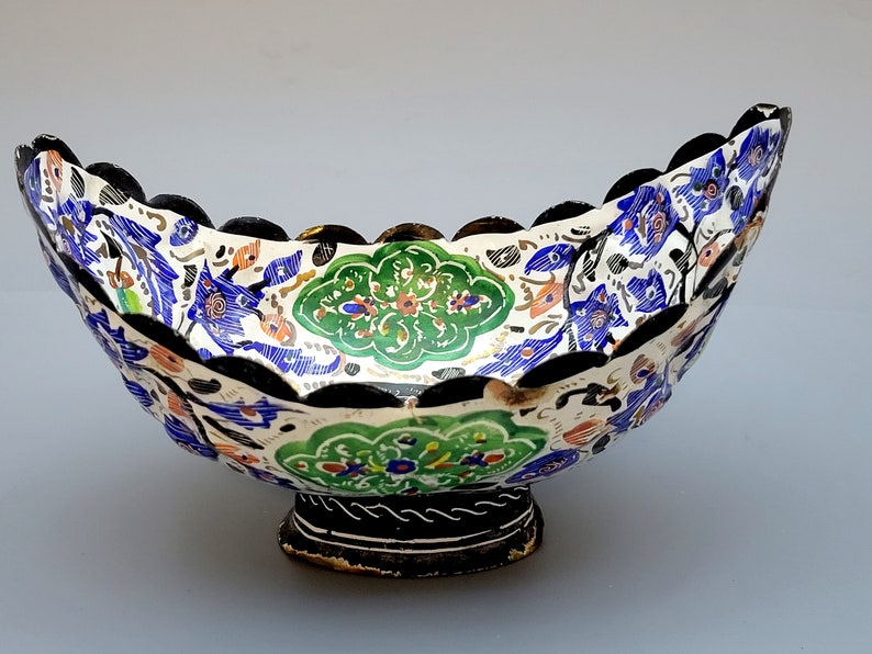 May include: A white ceramic bowl with a scalloped rim and a black base. The bowl is decorated with a colorful floral pattern in shades of blue, green, and gold.